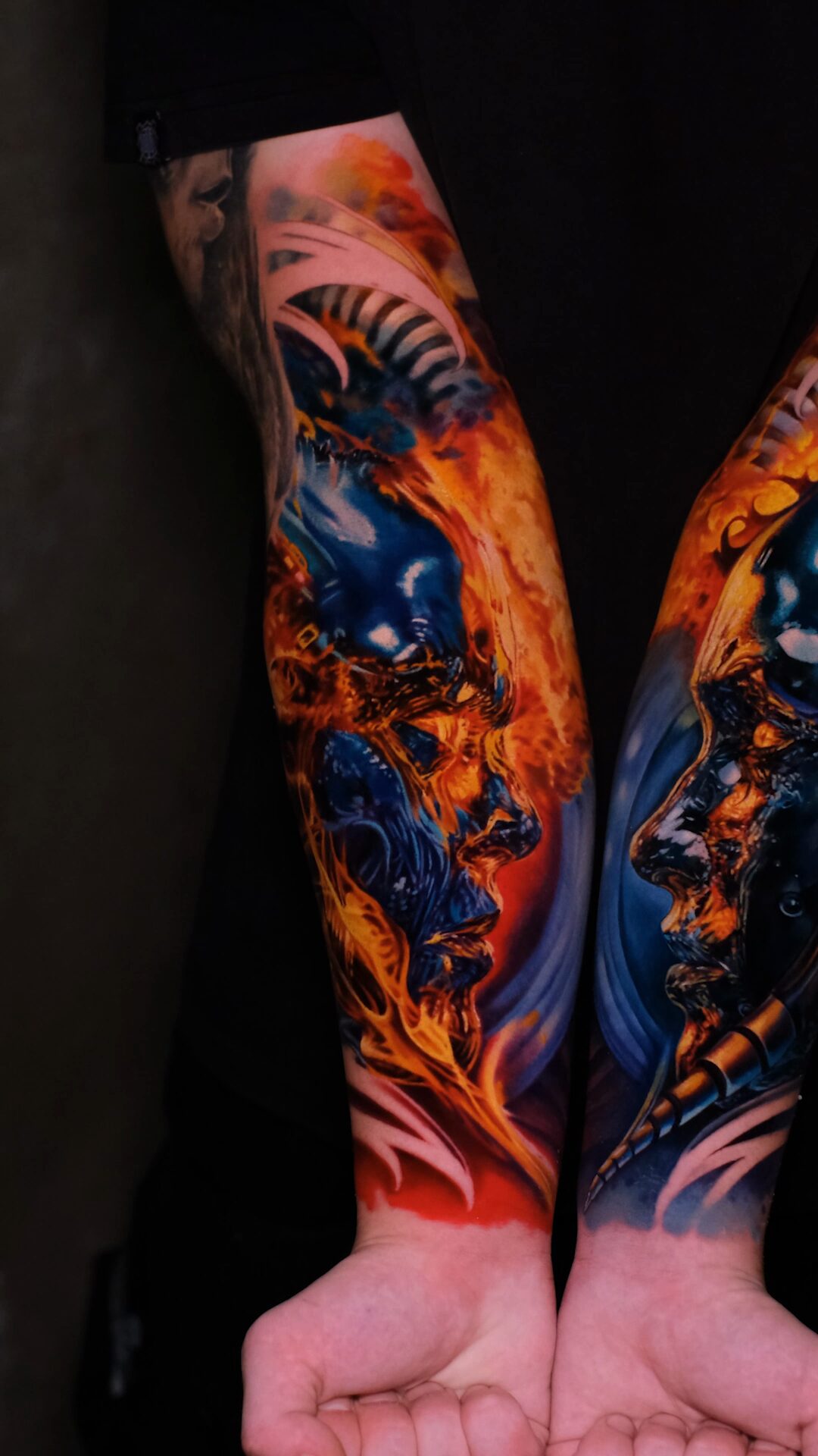 Biomechanisches Tattoo auf beiden Unterarmen – links im Feuer, rechts in Blau, Hände unten, Wrocław.