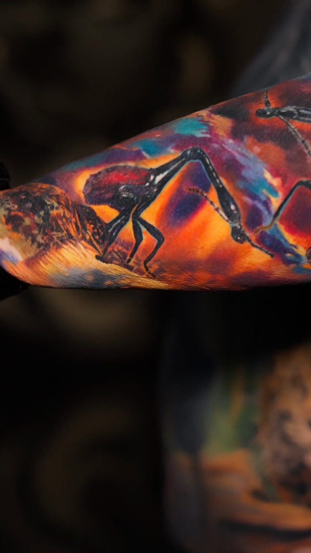 Unterarm von der Seite, großer Giraffenhalskäfer auf orange-violettem Hintergrund, Ellbogen links, Tätowierer Wrocław