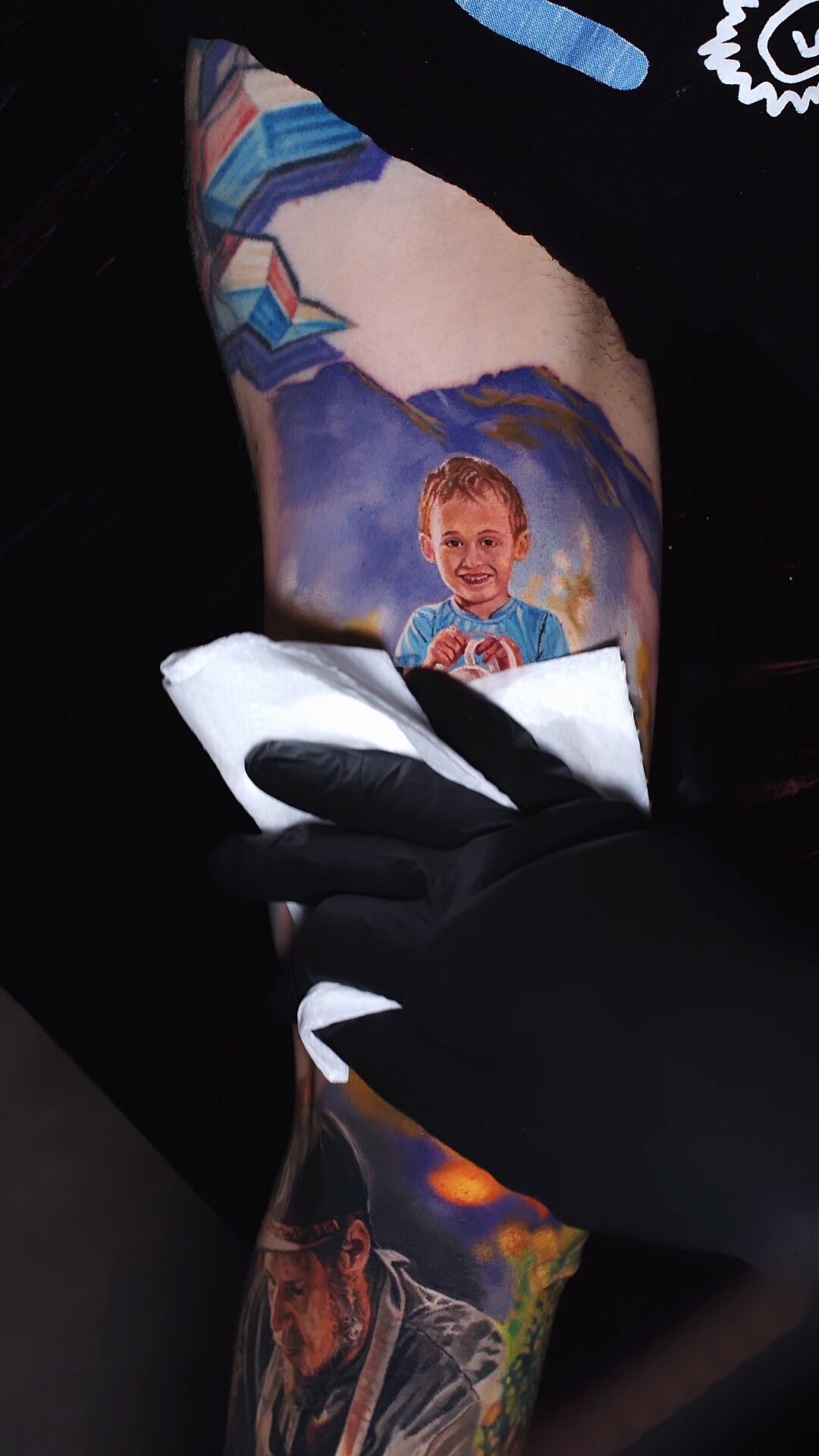 Fragment z drewnianym płotem i zielonym tłem – portret z fotografii, tatuaż na bicepsie, realizm
