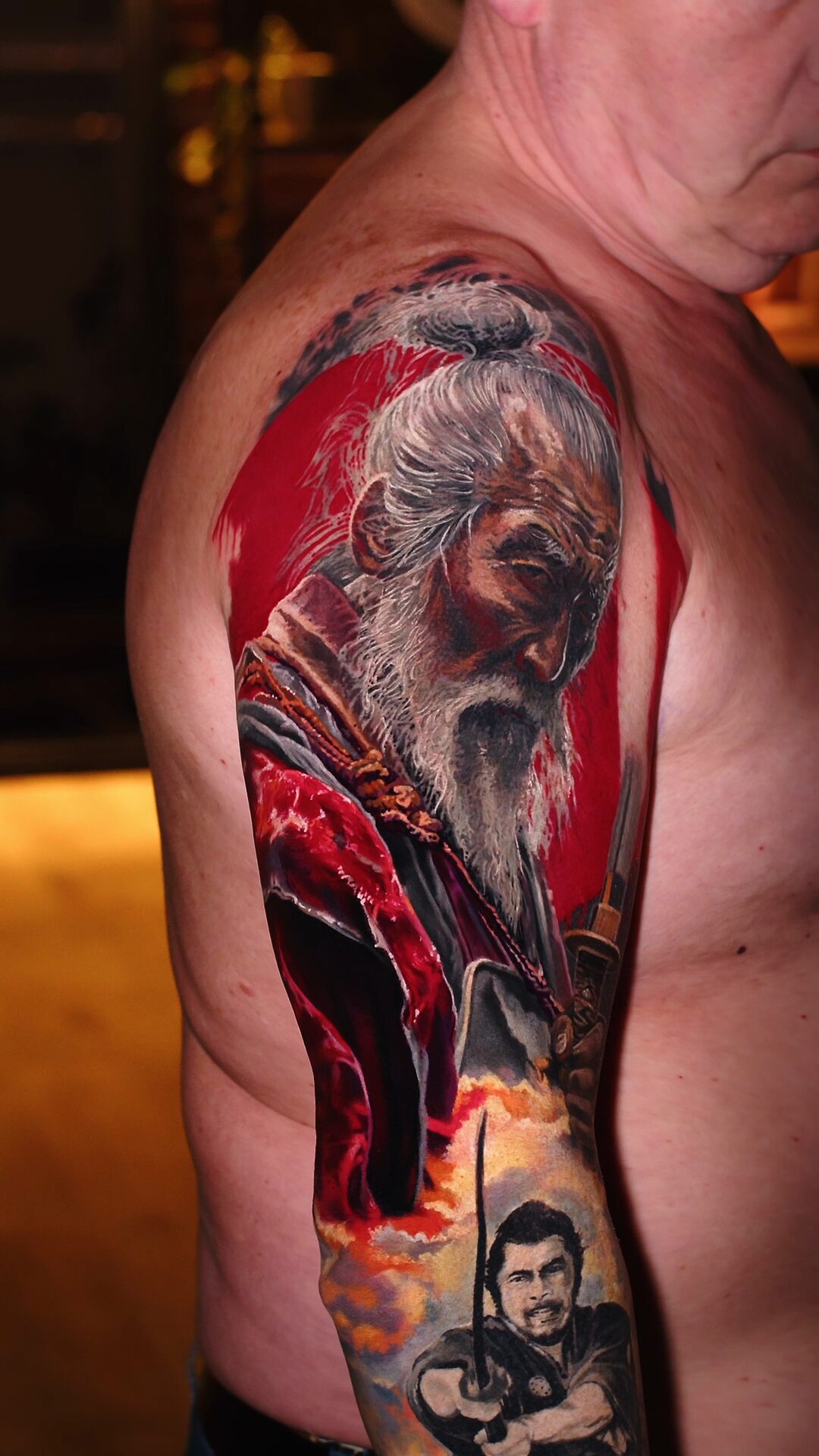 Samurai- und Meister-Tattoo am Oberarm – Color-Realism trifft black and grey