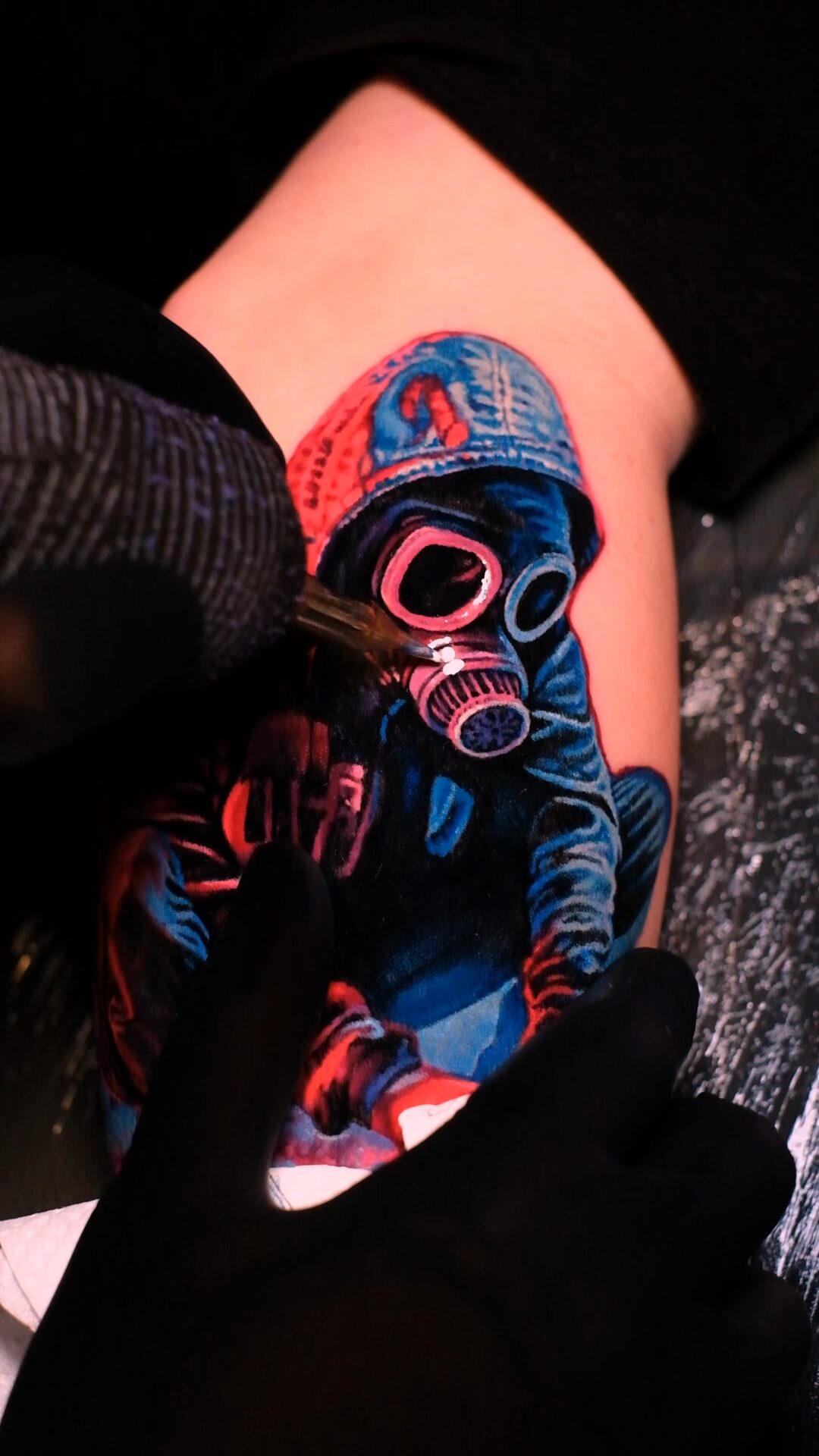 Während der Session: Hand im Handschuh an der Figur mit Gasmaske und Kapuze auf dem Oberarm, Tätowierer Wrocław.