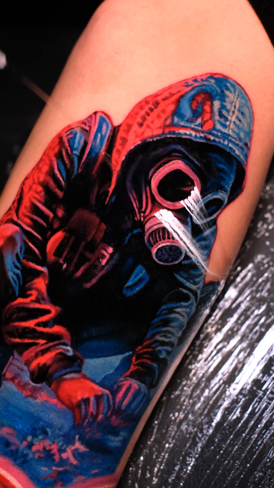 Tattoo einer Figur mit Gasmaske auf dem Oberarm – blauer Grund und rosa Neonlichtstreifen.