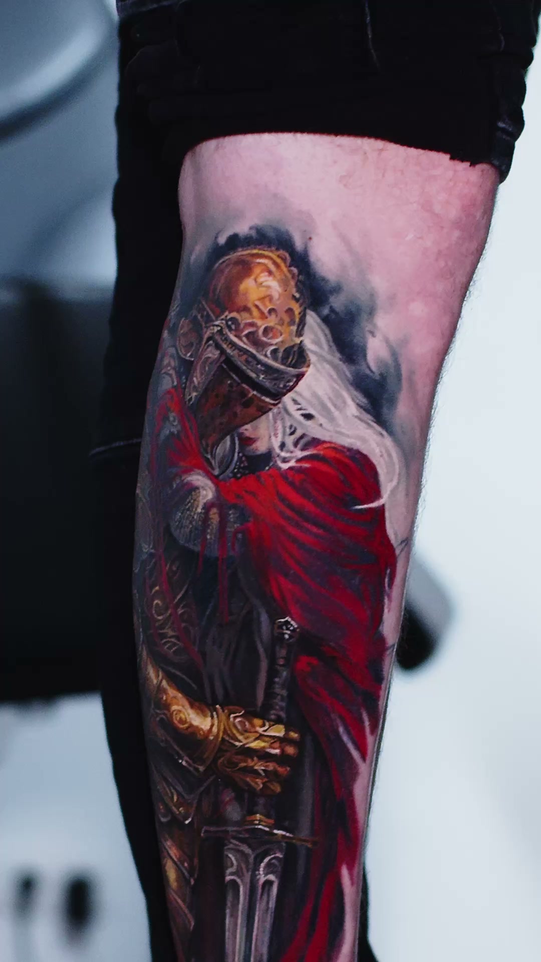Oberer Teil des Tattoos auf der Wade: goldener Helm mit geschlossenem Visier, weiße Haare und roter Umhang, Tätowierer Wrocław.