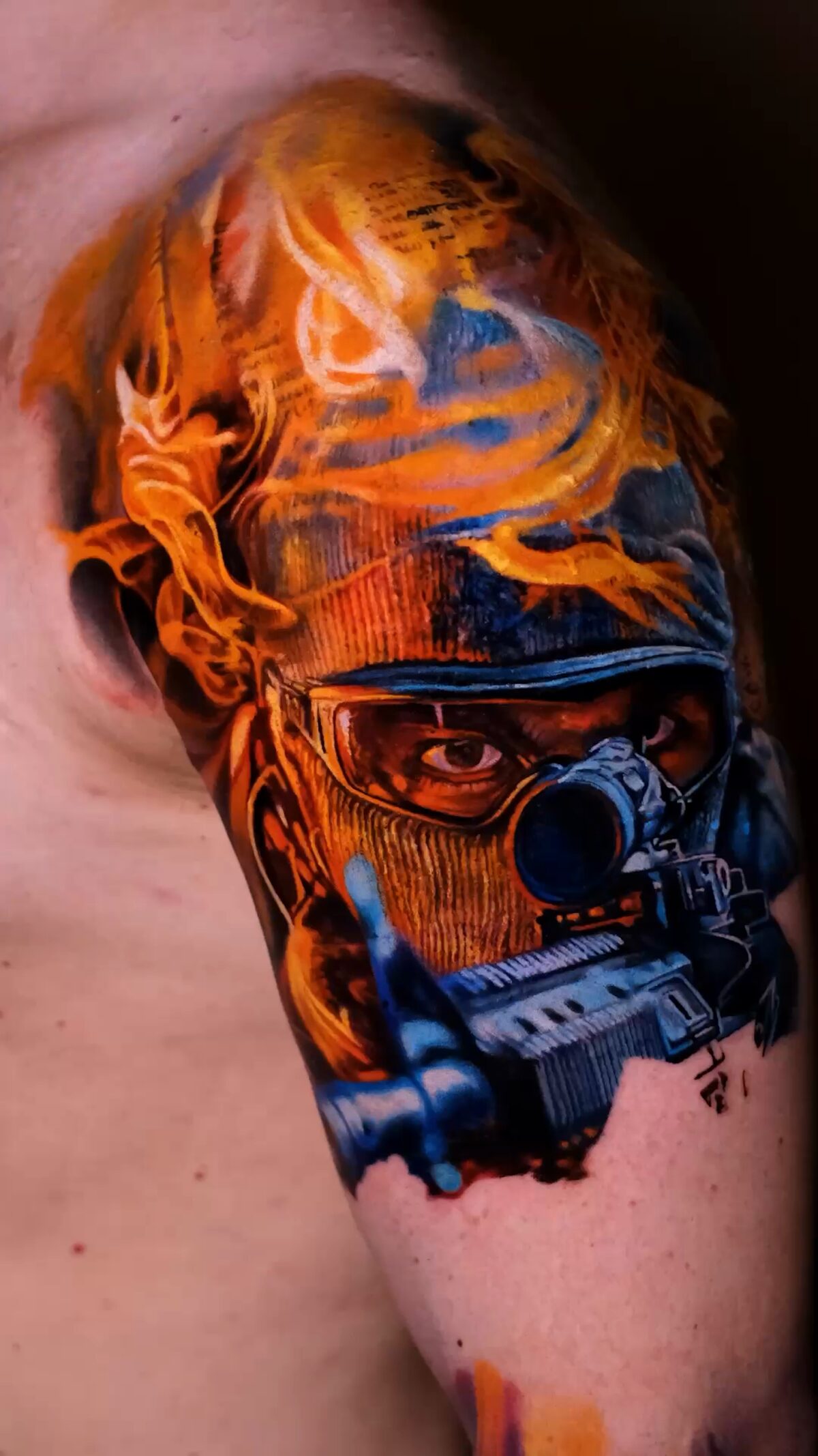Gesamtes Soldaten-Tattoo auf der Schulter – türkise Sturmhaube, Schutzbrille, Gewehrmündung auf den Betrachter, orangefarbenes Feuer, Tätowierer Wrocław.
